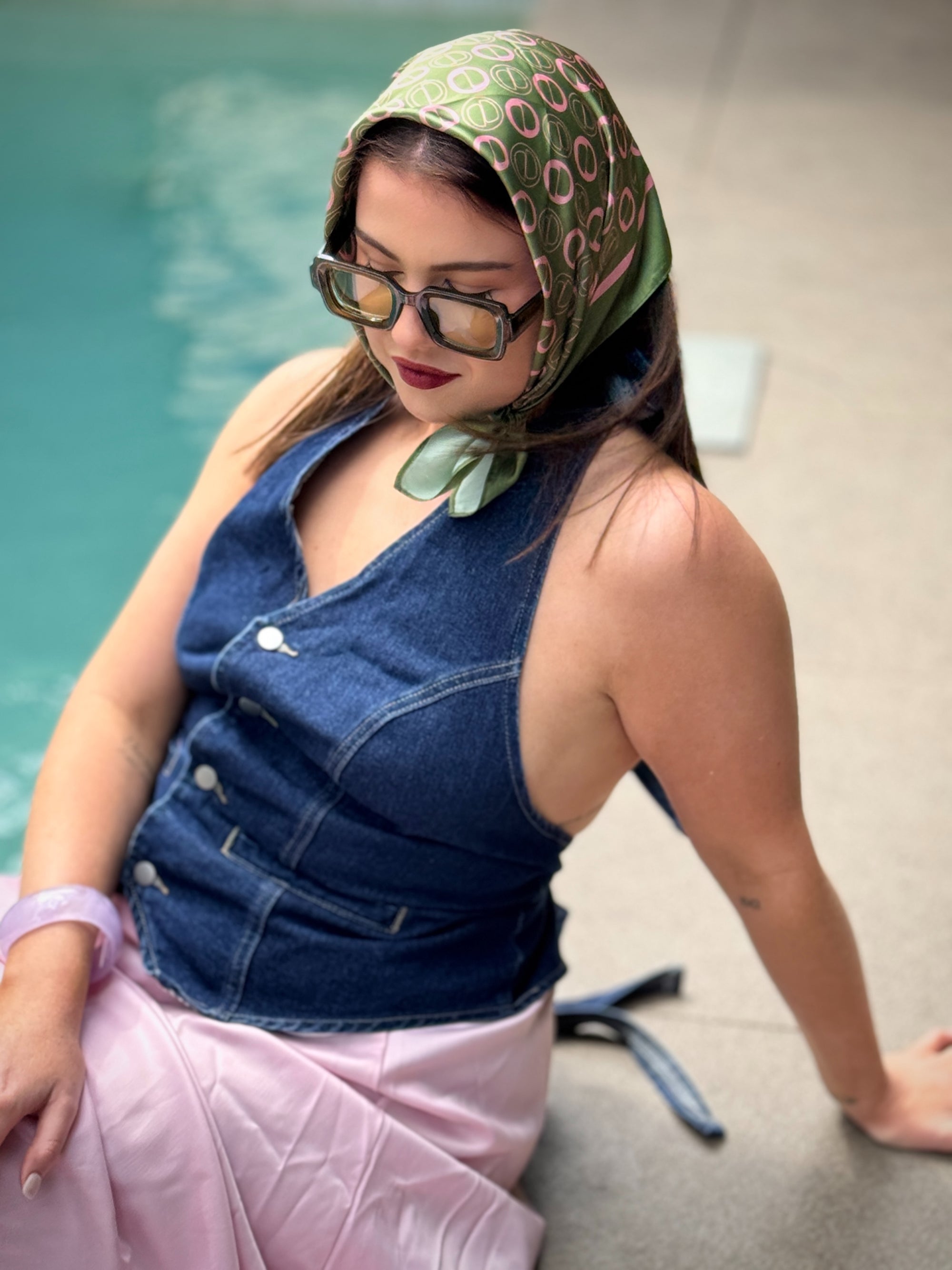 Woman wearing a denim vest and green patterned headscarf by a pool.