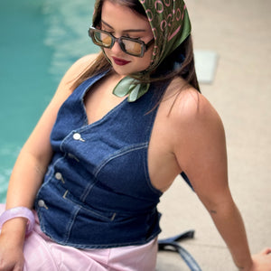 Woman wearing a denim vest and green patterned headscarf by a pool.